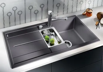 A modern kitchen sink with a faucet and two green apples in a small inset basin.