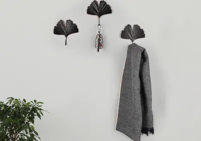Three ginkgo leaf-shaped hooks on a wall, with keys hanging from one and a scarf from another. A plant is in the lower left corner.