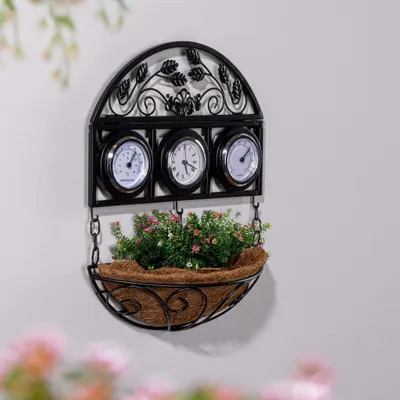 A black metal wall-mounted planter with three thermometers and a basket filled with green plants and pink flowers.