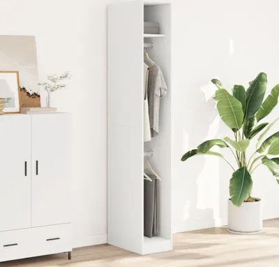 A white wardrobe with clothes hanging inside, next to a white cabinet and a large potted plant.