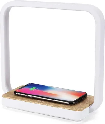 A white LED lamp with a wooden base and a smartphone charging on it.