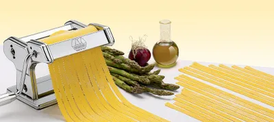 A pasta maker is shown with fresh pasta being extruded, alongside asparagus, a red onion, and a bottle of olive oil.