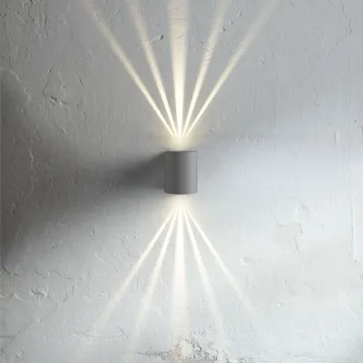 A grey cylindrical wall light mounted on a textured white wall, casting beams of light upwards and downwards.