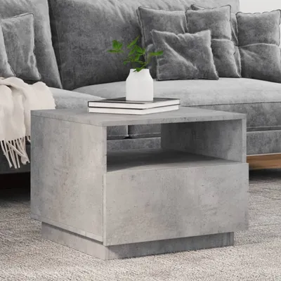 A concrete-look side table sits next to a gray sofa with pillows and a blanket.