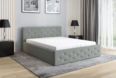 A grey upholstered bed with a mattress and a bedside table with a lamp.