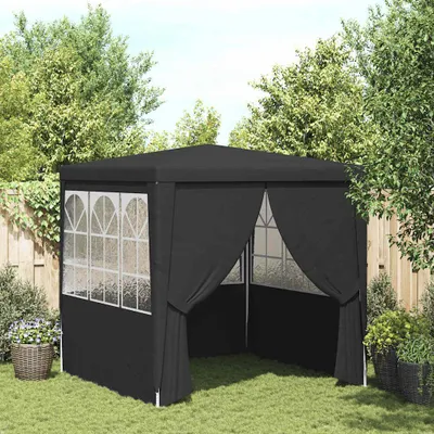 A black party tent set up on a grassy lawn in a backyard, surrounded by trees and a wooden fence.