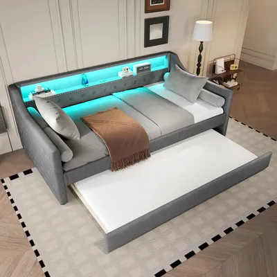 A gray daybed with a pull-out trundle bed, illuminated by blue LED lights.