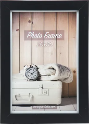 A black photo frame with a wooden background, a white suitcase, and a knitted blanket with an alarm clock on top.