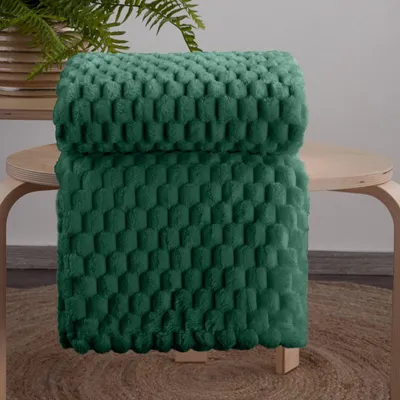 A folded dark green blanket with a textured pattern is placed on a wooden stool.