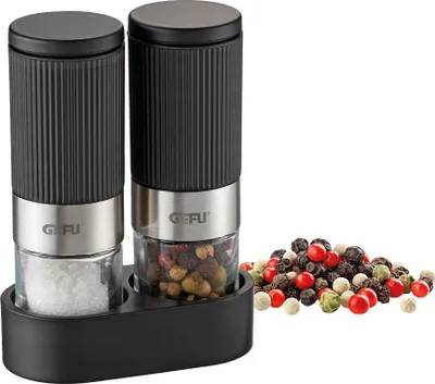 A set of salt and pepper grinders with a pile of peppercorns next to them.