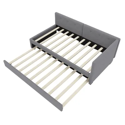 A gray upholstered daybed with a pull-out trundle bed frame extended.