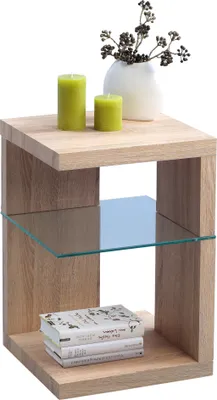 A wooden side table with two green candles, a white vase with decorative branches, and a stack of books.
