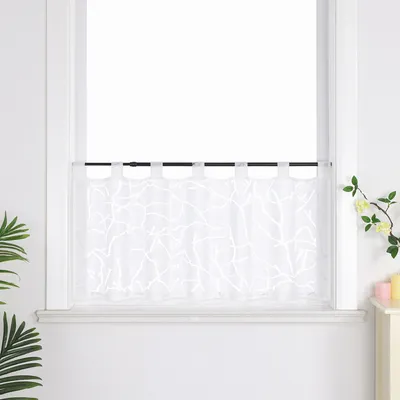 A white voile cafe curtain with a branch pattern hangs on a black rod in a window.