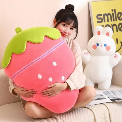 A woman is sitting on a couch, holding a large strawberry plush toy. A white rabbit plush toy is visible in the background.