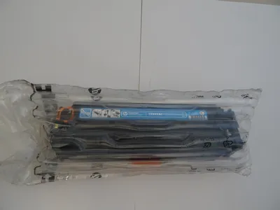A toner cartridge sealed in plastic packaging, lying flat on a white and light gray background.