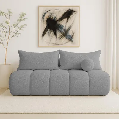 A modern living room scene featuring a gray bouclé sofa with decorative pillows and a piece of abstract art on the wall.