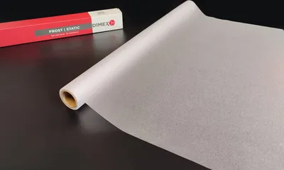 A roll of translucent window film is shown on a dark surface, with its packaging in the background.