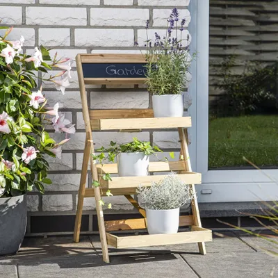 A wooden plant stand with three shelves, holding potted plants, placed outdoors against a brick wall.