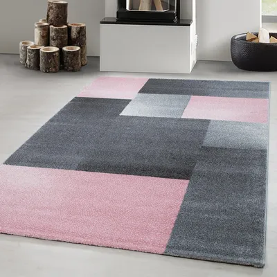 A modern abstract rug with geometric patterns in pink and gray, placed on a light gray floor.