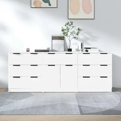A white sideboard with black handles and drawers is placed on a gray geometric rug in front of a white wall. Two abstract paintings hang on the wall.