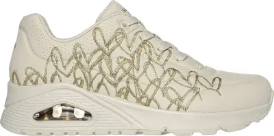 A side view of a cream-colored Skechers sneaker with a gold heart pattern.
