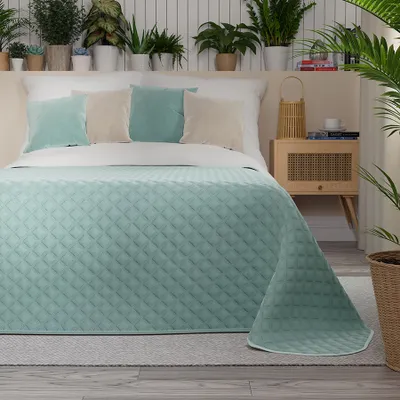 A bed with a mint green quilted bedspread and decorative pillows.