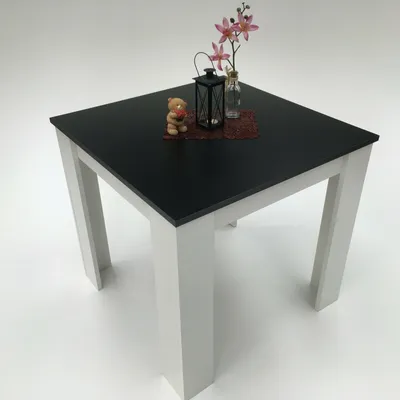 A square table with a black top and white legs, set against a white background. Decorative items are placed on the table.
