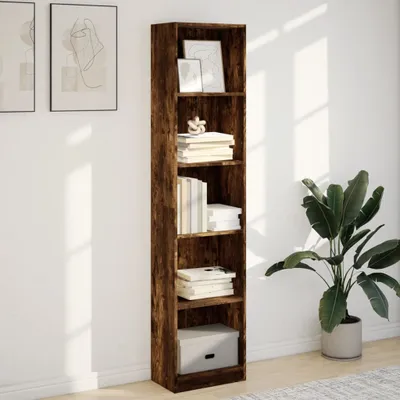 A tall, narrow bookshelf with a dark wood finish, filled with books and decorative items, stands against a white wall. A large potted plant is to the right of the bookshelf.
