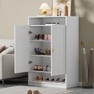 A white shoe cabinet with two doors, filled with shoes and a lamp on top.