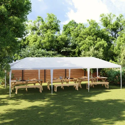 A white party tent set up in a grassy backyard with picnic tables and benches underneath.