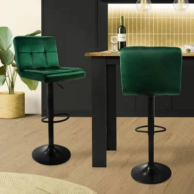 Two green velvet bar stools are shown in a modern kitchen setting, with a bottle of wine and glasses on the counter.
