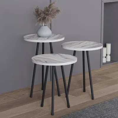 Three nesting side tables with marble-look tops and black metal legs are arranged in a living room setting against a gray wall.