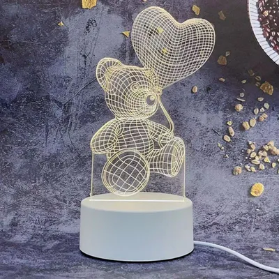 A 3D wireframe teddy bear holding a heart-shaped balloon, illuminated by internal lights, sits on a white base with a power cord.