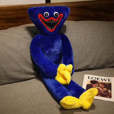 A large blue plush toy with yellow hands and feet is sitting on a gray sofa next to a magazine.