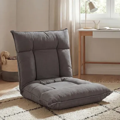 A dark gray floor chair is placed on a rug in a room with a desk and window in the background.