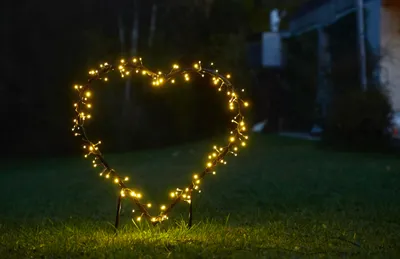 A heart-shaped light decoration with yellow LEDs is placed on a lawn at night.