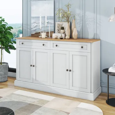 A white sideboard with a wood top is displayed in a room with a plant, artwork, and decorative vases on top. A rug is on the floor in front of it.