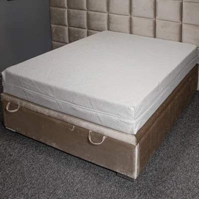 A mattress on a bed base with a headboard in the background.