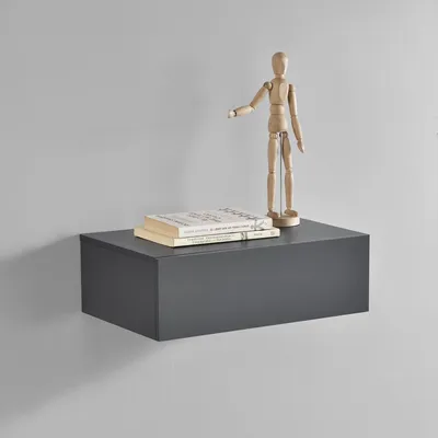 A dark gray floating shelf with two books and a wooden mannequin on it, against a light gray wall.