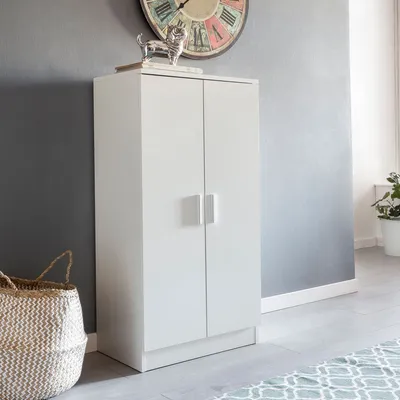 A white two-door cabinet stands against a gray wall, with a woven basket to its left and a large clock on the wall above.