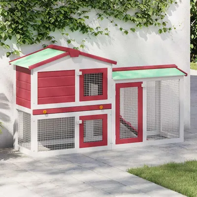 A red and white wooden rabbit hutch with a green roof sits on a paved patio, with ivy growing on a white wall behind it.