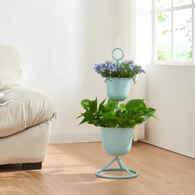 A light blue two-tiered plant stand with green and purple plants sits on a wooden floor next to a cream-colored sofa, with a window in the background.
