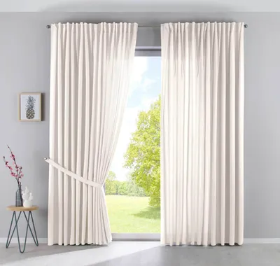 A room with a large window covered by cream-colored curtains. A small side table with decorative items is placed to the left of the curtains.