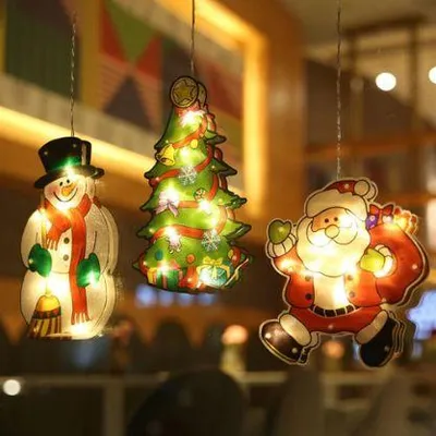Drei beleuchtete Weihnachtsfensterlichter: ein Schneemann, ein Weihnachtsbaum und der Weihnachtsmann, hängend vor einem unscharfen Hintergrund