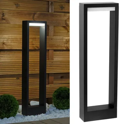 A modern black outdoor bollard light with a white LED light strip, shown in a garden setting with a wooden fence and decorative stones.