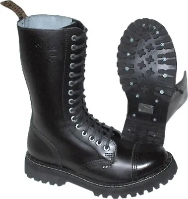 A pair of black leather boots with steel toes and a thick sole, shown from a slightly angled front view. One boot is upright, and the other is shown sole-up, revealing the studded tread.