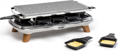 A Tefal raclette grill with a stone cooking surface and multiple small pans underneath, shown on a white background with two extra pans in the foreground.