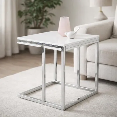 A white side table with a chrome frame is placed on a rug next to a sofa. A pink vase and a white bird figurine are on the table.