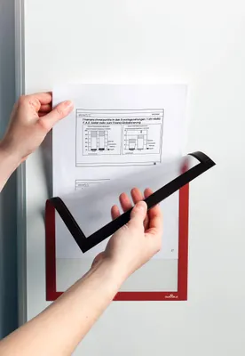 Hands holding a document over a red magnetic frame attached to a white surface.