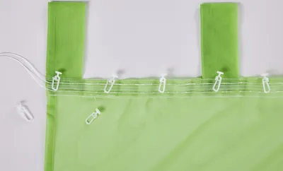 A close-up view of a green translucent curtain with white clips attached along the top edge.